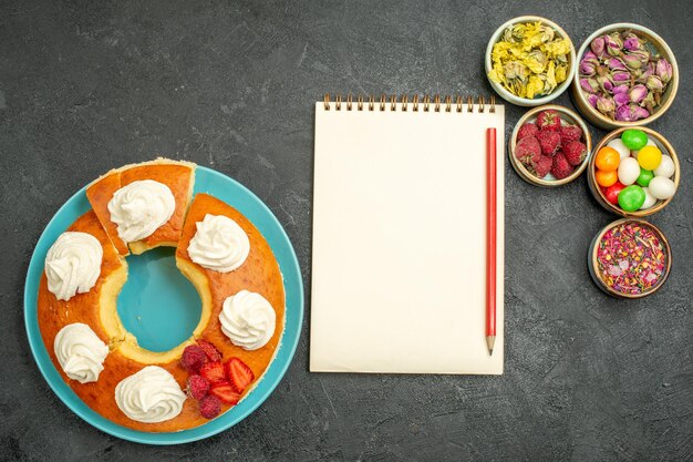 Vue de dessus d'une délicieuse tarte à la crème avec des fleurs et des bonbons sur fond noir