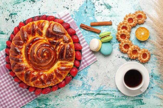 Vue de dessus délicieuse tarte avec des macarons de biscuits aux fraises rouges fraîches et tasse de thé sur la surface bleue