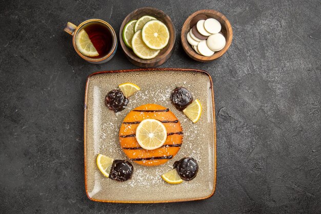 Vue de dessus délicieuse tarte sucrée avec des tranches de citron et une tasse de thé sur le fond gris gâteau tarte biscuit biscuit sucré