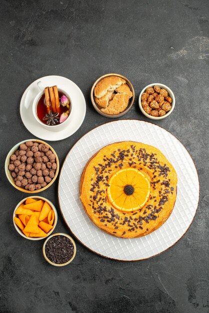 Vue de dessus délicieuse tarte sucrée avec des tranches d'orange et une tasse de thé sur une surface sombre biscuits tarte biscuit dessert gâteau au thé