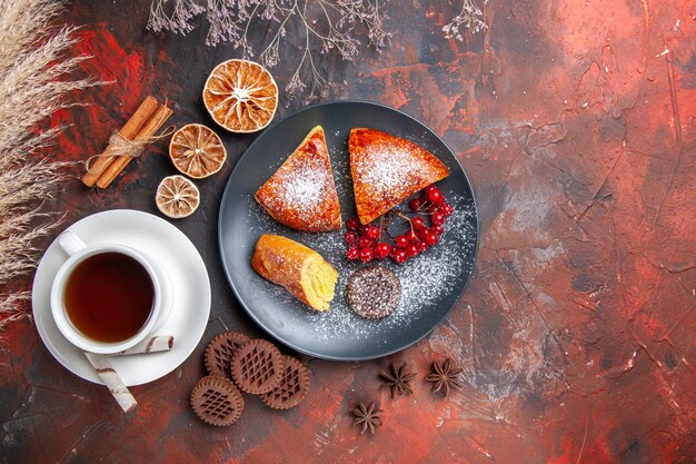 Vue de dessus délicieuse tarte en tranches avec une tasse de thé sur un gâteau de bureau sombre thé à tarte sucrée