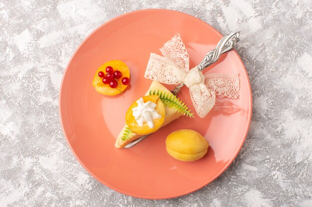 Vue de dessus délicieuse tranche de gâteau avec des abricots à la crème à l'intérieur de la plaque rose sur le gâteau de bureau lumineux pâte sucrée au sucre