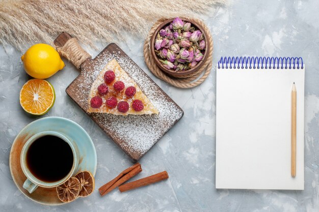 Vue de dessus délicieuse tranche de gâteau avec une tasse de thé et de citrons bloc-notes sur le bureau léger gâteau biscuit sucre sucré cuire