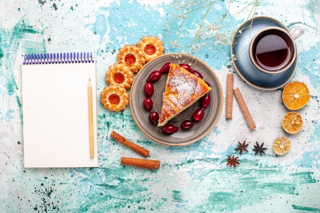 Vue de dessus délicieuse tranche de gâteau avec une tasse de thé sur le gâteau de bureau bleu cuire au four tarte biscuit sucré