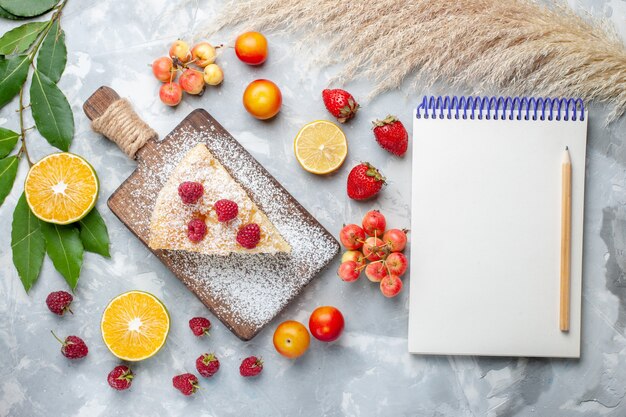 Vue de dessus délicieuse tranche de tarte délicieuse avec des fruits et bloc-notes sur un bureau léger biscuit gâteau tarte sucrée au sucre