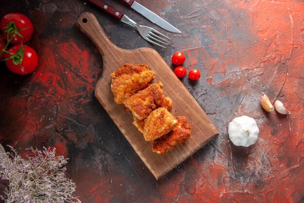 Vue de dessus de délicieuses ailes de poulet sur une planche à découper avec une surface sombre de tomates