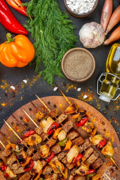 Vue de dessus de délicieuses brochettes de poulet sur planche de bois sur table sombre