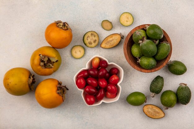 Vue de dessus de délicieuses cerises cornaline sur un bol avec feijoas sur un bol en bois avec kaki isolé sur un mur gris