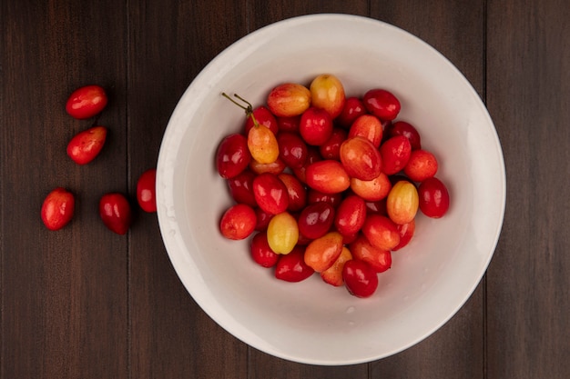 Photo gratuite vue de dessus de délicieuses cerises cornaline rouge sur un bol blanc sur un mur en bois