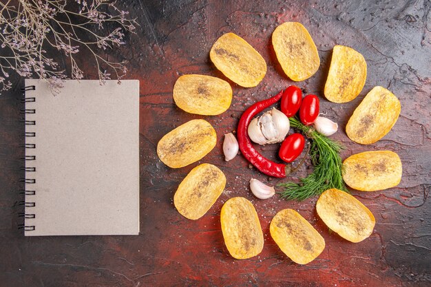 Vue de dessus de délicieuses chips croustillantes faites maison poivron rouge ail tomates vertes et cahier sur table sombre