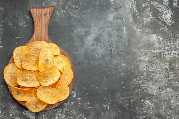 Vue de dessus de délicieuses chips maison sur une planche à découper en bois sur fond gris