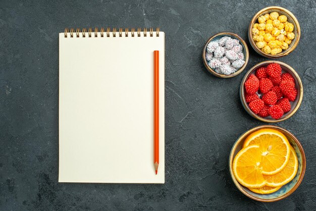 Vue de dessus de délicieuses confitures avec des tranches d'orange et un bloc-notes sur une surface sombre confiture de fruits bonbon au sucre