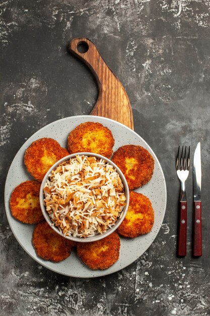 Vue de dessus de délicieuses côtelettes frites avec du riz cuit sur la rissole de viande de plat de surface sombre