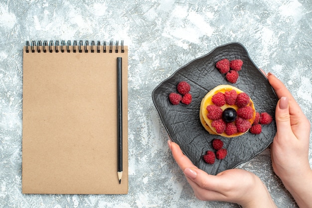 Vue de dessus de délicieuses crêpes aux framboises et bloc-notes sur fond clair