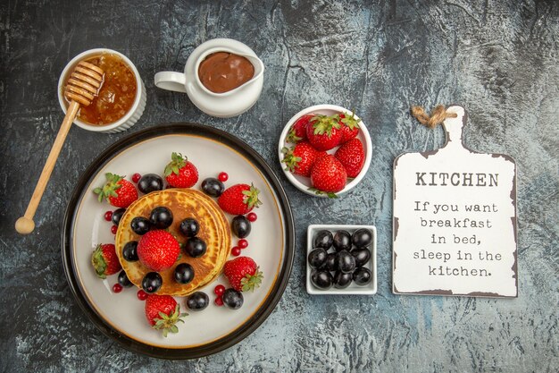 Vue de dessus de délicieuses crêpes aux fruits frais et au miel sur un gâteau aux fruits sucrés au sol léger