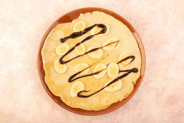Photo gratuite une vue de dessus de délicieuses crêpes conçues avec du chocolat et des bananes à l'intérieur de la plaque ronde sur le bureau rose pâtisserie dessert repas alimentaire