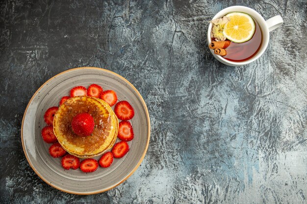 Vue de dessus de délicieuses crêpes avec des fraises et une tasse de thé à la lumière