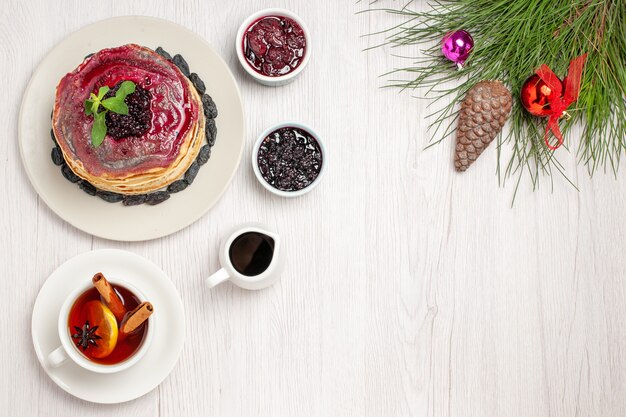 Vue de dessus de délicieuses crêpes à la gelée avec de la gelée fruitée aux raisins secs et une tasse de thé sur blanc clair