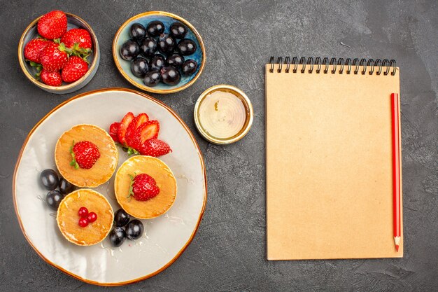 Vue de dessus de délicieuses crêpes peu formées avec des fruits sur un gâteau aux fruits à tarte au sol gris