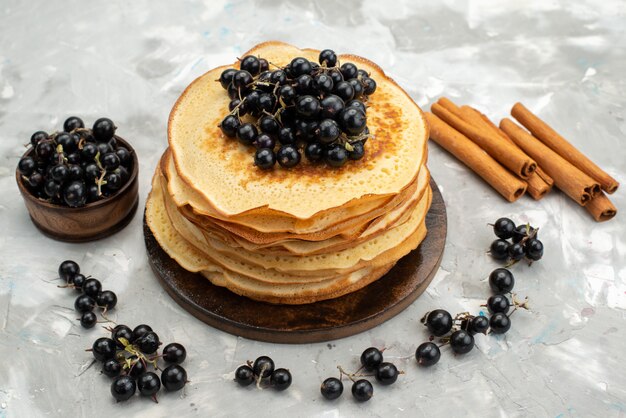 Une vue de dessus de délicieuses crêpes rondes délicieuses et rondes formées de myrtilles et de cannelle sur le bureau léger