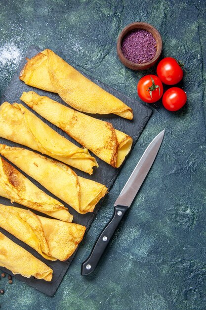 Vue de dessus de délicieuses crêpes roulées bordées de tomates sur fond sombre couleur repas tarte pâte à viande gâteau sucré pâtisserie