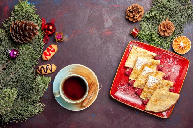 Vue de dessus de délicieuses crêpes sucrées aux framboises et tasse de thé sur fond noir