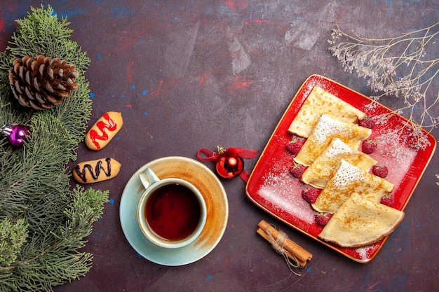 Vue de dessus de délicieuses crêpes sucrées aux framboises et thé sur table noire