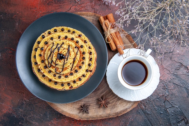 Photo gratuite vue de dessus de délicieuses crêpes sucrées avec une tasse de thé sur une surface sombre