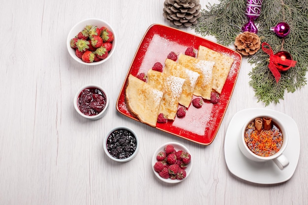 Vue de dessus de délicieuses crêpes avec tasse de thé et fruits sur blanc