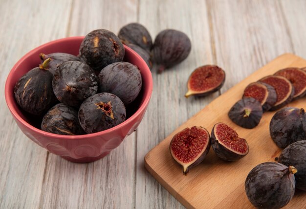 Vue de dessus de délicieuses figues de mission noires mûres sur une planche de cuisine en bois avec des figues noires sur un bol sur une surface en bois gris