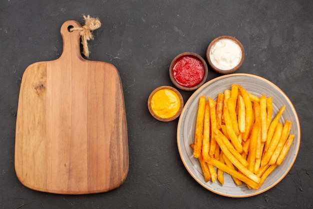 Vue de dessus de délicieuses frites avec des assaisonnements sur fond sombre plat de burger fast-food de pommes de terre