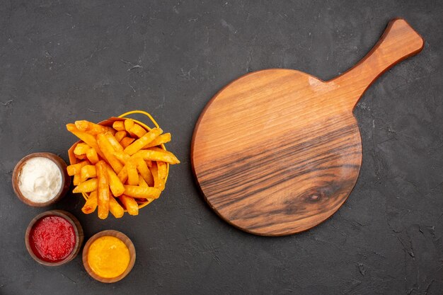 Vue de dessus de délicieuses frites avec des assaisonnements sur fond sombre plat de pommes de terre fast-food burger repas