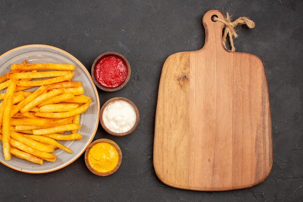 Vue de dessus de délicieuses frites avec des assaisonnements sur fond sombre plat de repas de hamburger de restauration rapide de pommes de terre