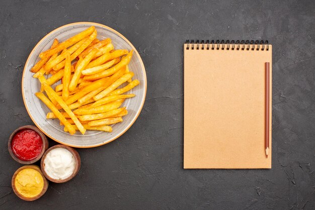 Vue de dessus de délicieuses frites avec des assaisonnements sur fond sombre plat de repas de pommes de terre burger fast-food