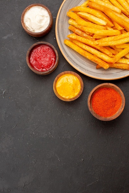 Vue de dessus de délicieuses frites avec des assaisonnements sur fond sombre repas fast-food plat de pommes de terre burger