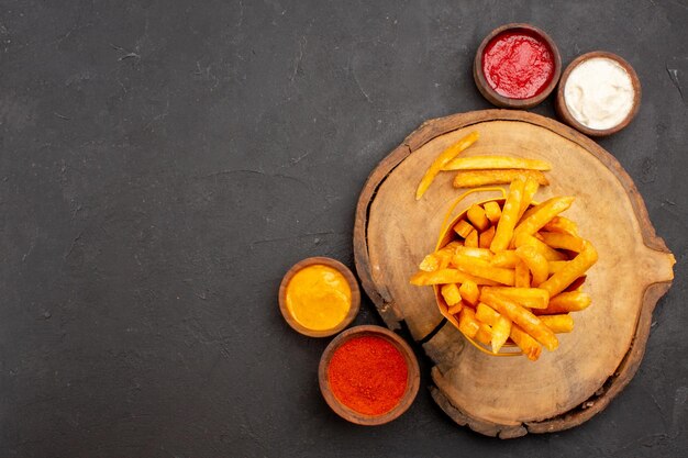 Vue de dessus de délicieuses frites avec des sauces dans l'obscurité