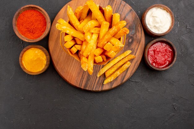 Vue de dessus de délicieuses frites avec des sauces sur fond noir