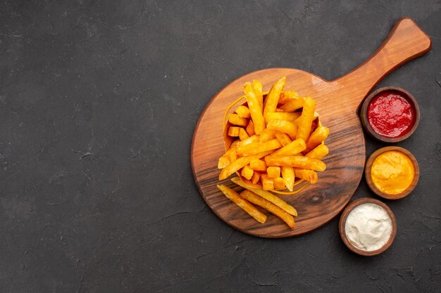 Vue de dessus de délicieuses frites avec des sauces sur fond noir