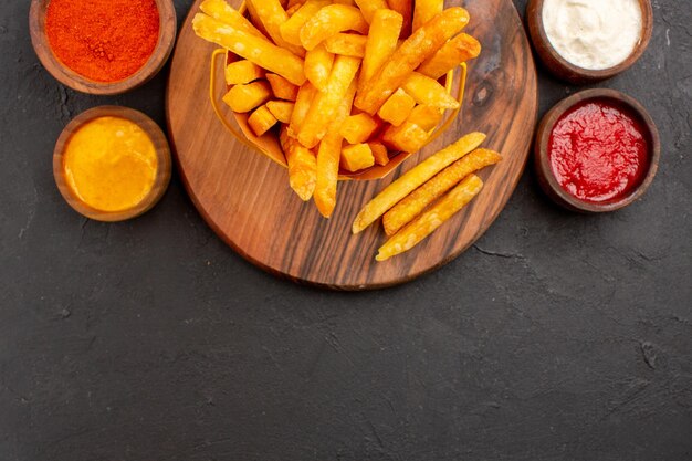 Vue de dessus de délicieuses frites avec des sauces sur fond noir