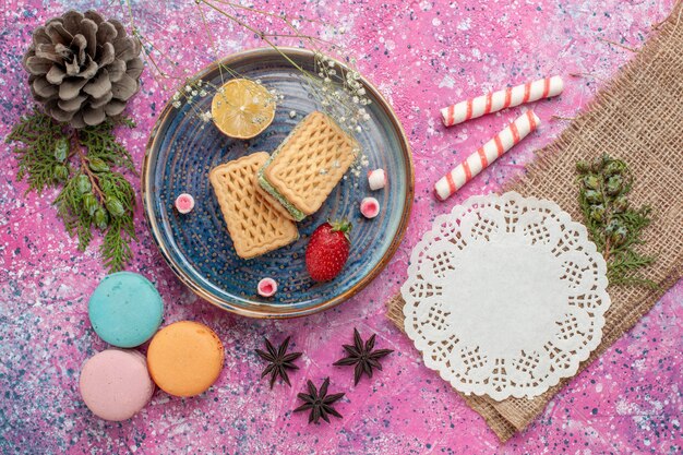 Vue de dessus de délicieuses gaufres avec des macarons français sur un bureau rose