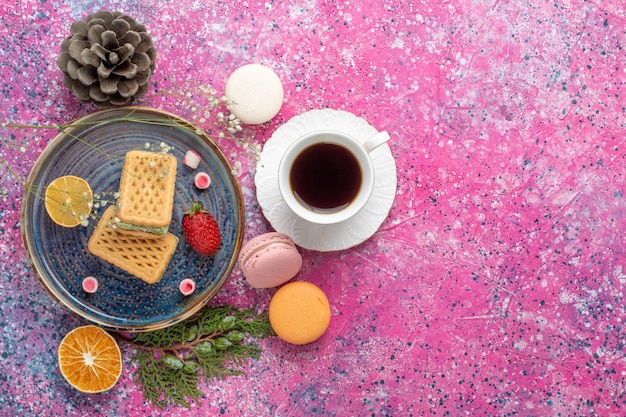 Photo gratuite vue de dessus de délicieuses gaufres avec des macarons français et du thé sur la surface rose