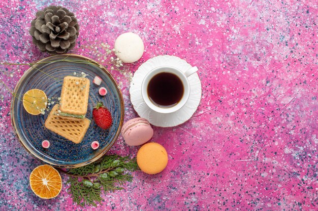 Vue de dessus de délicieuses gaufres avec des macarons français et du thé sur la surface rose