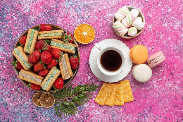 Vue de dessus de délicieuses gaufres avec tasse de macarons au thé et fraises rouges fraîches sur surface rose