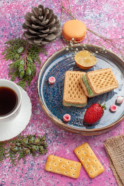 Vue de dessus de délicieuses gaufres avec une tasse de thé sur un bureau rose