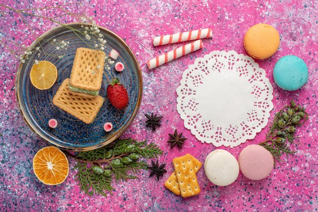 Vue de dessus de délicieuses gaufres avec tasse de thé et macarons sur surface rose