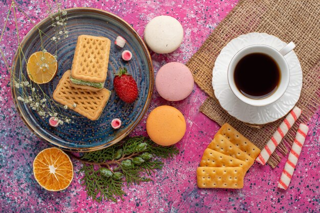 Vue de dessus de délicieuses gaufres avec thé macarons et guimauve sur la surface rose clair