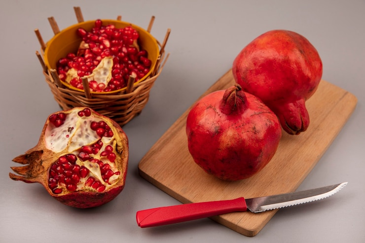 Photo gratuit vue de dessus de délicieuses grenades rouges sur une planche de cuisine en bois avec un couteau avec des graines de grenade sur un bol