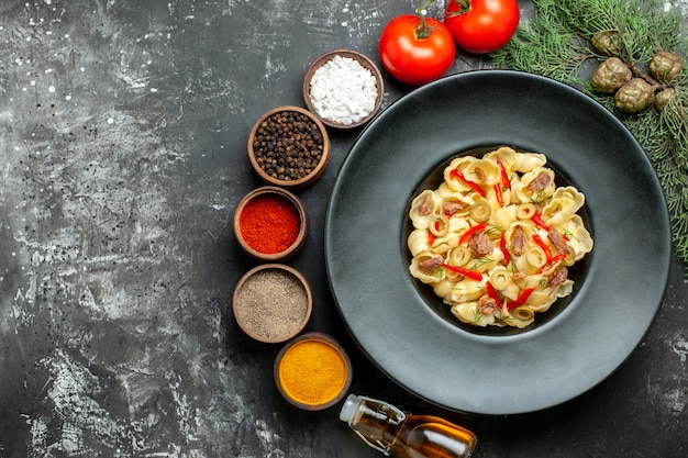 Vue de dessus de délicieuses pâtes aux légumes verts sur une assiette et un couteau et différentes épices bouteille d'huile tombée sur une table grise