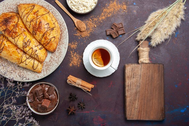 Vue de dessus de délicieuses pâtisseries cuites au four avec du fromage cottage et du thé sur l'espace sombre