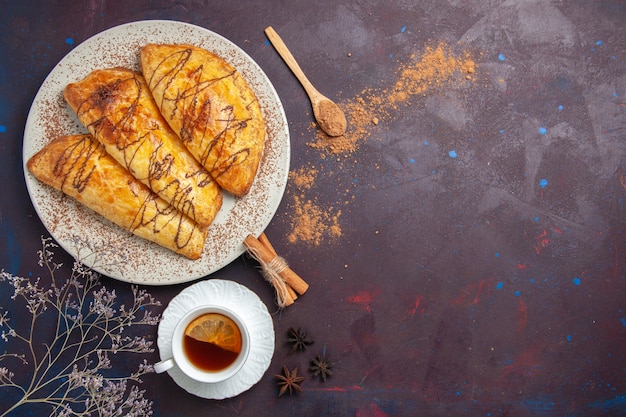 Vue de dessus de délicieuses pâtisseries cuites au four avec une tasse de thé sur l'espace sombre